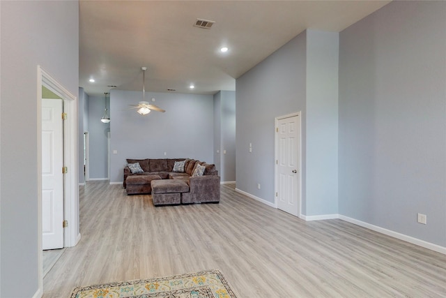 living room featuring ceiling fan, a towering ceiling, and light wood-type flooring