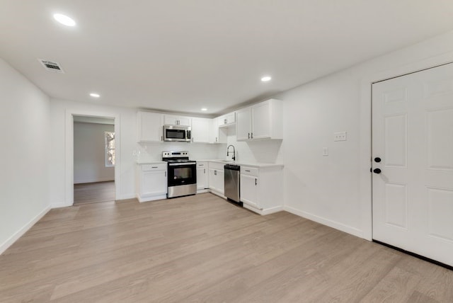 kitchen featuring appliances with stainless steel finishes, light wood-type flooring, white cabinets, and backsplash