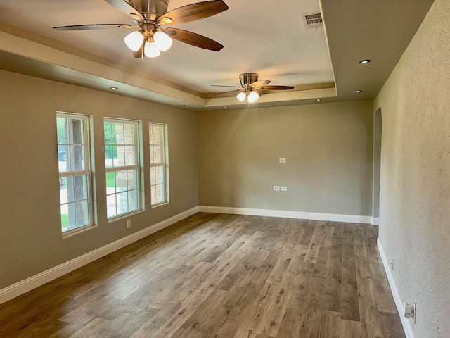 empty room with light hardwood / wood-style floors, a raised ceiling, and ceiling fan