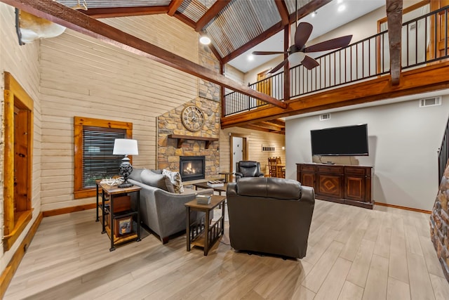 living room featuring beam ceiling, wooden walls, high vaulted ceiling, a fireplace, and light wood-type flooring