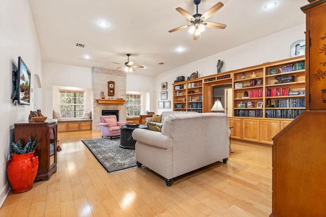 living room with ceiling fan, a large fireplace, and light hardwood / wood-style floors