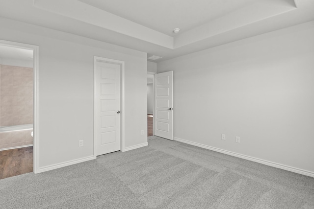 unfurnished bedroom with a raised ceiling, light carpet, baseboards, and ensuite bathroom