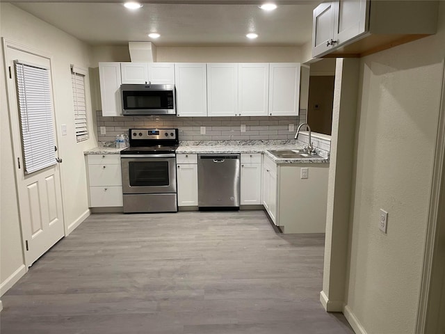 kitchen with sink, white cabinets, stainless steel appliances, light hardwood / wood-style floors, and backsplash