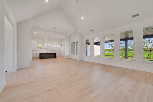 unfurnished living room featuring light wood-style floors, high vaulted ceiling, visible vents, and an inviting chandelier
