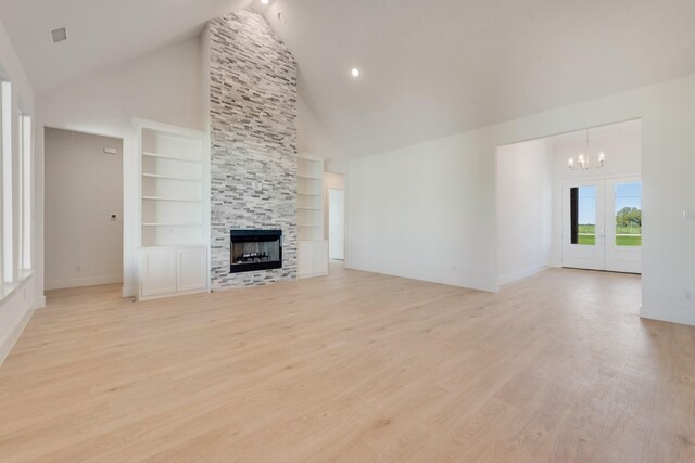 unfurnished living room with a notable chandelier, a stone fireplace, light wood-style floors, high vaulted ceiling, and built in shelves