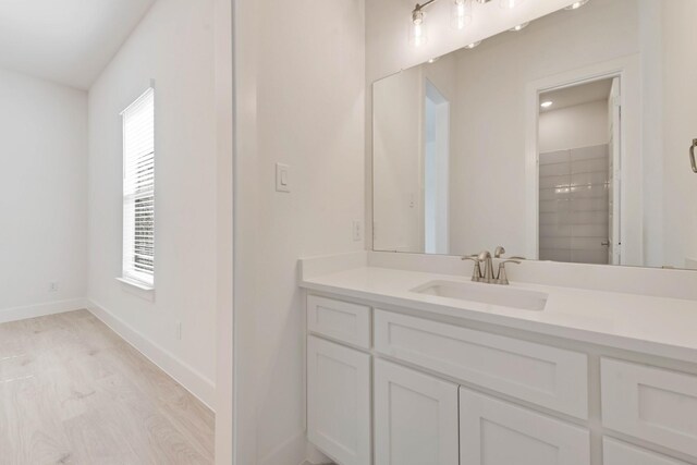 bathroom featuring baseboards, a shower, vanity, and wood finished floors