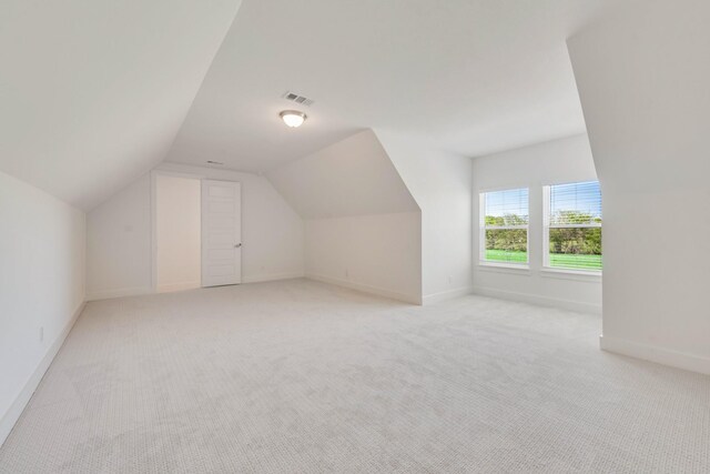 additional living space with light carpet, visible vents, baseboards, and vaulted ceiling