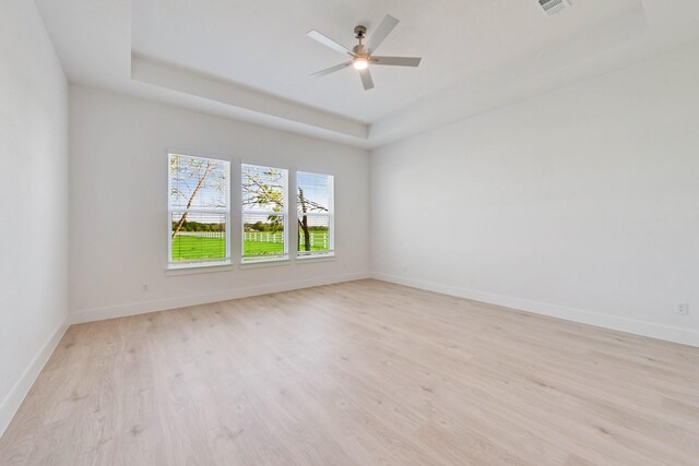 empty room featuring a tray ceiling, light wood-style flooring, ceiling fan, and baseboards