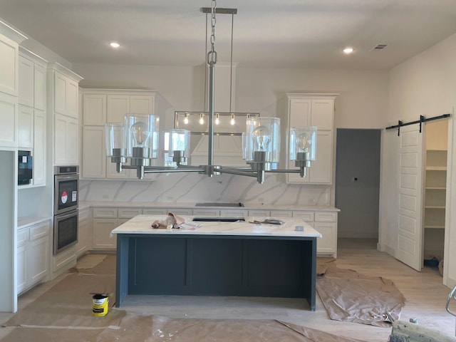 kitchen with visible vents, light countertops, a barn door, stainless steel double oven, and white cabinetry