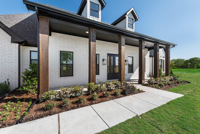 view of front of home featuring roof with shingles, french doors, a front lawn, brick siding, and covered porch