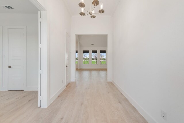 hallway featuring baseboards, an inviting chandelier, ornamental molding, visible vents, and light wood finished floors