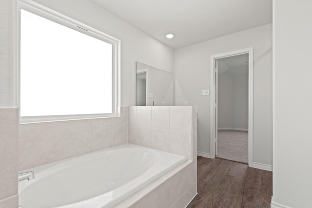 bathroom with a relaxing tiled tub and wood-type flooring