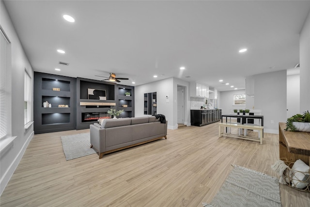 living room with ceiling fan, sink, built in features, and light wood-type flooring