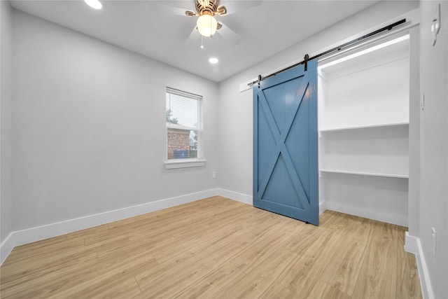 empty room featuring ceiling fan, a barn door, and light hardwood / wood-style floors