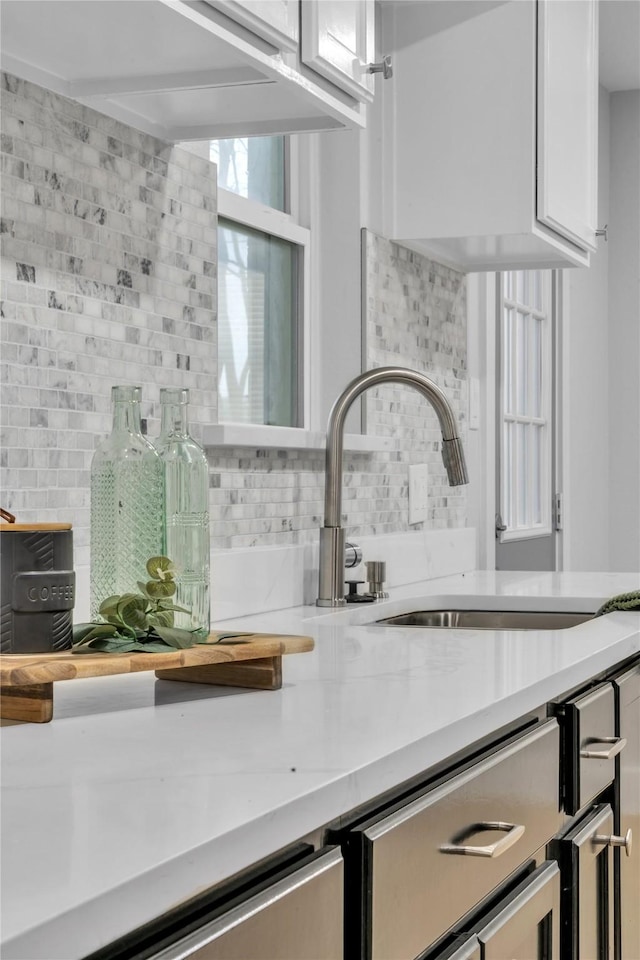 interior details featuring white cabinetry, sink, light stone counters, and tasteful backsplash