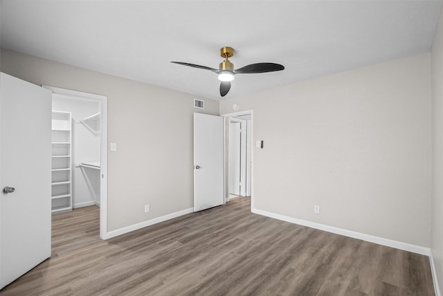 unfurnished bedroom with a walk in closet, wood-type flooring, a closet, and ceiling fan