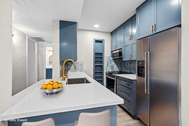 kitchen with sink, blue cabinetry, appliances with stainless steel finishes, a kitchen breakfast bar, and tasteful backsplash