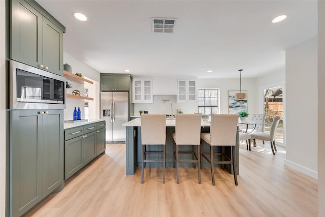 kitchen featuring pendant lighting, green cabinetry, appliances with stainless steel finishes, and light hardwood / wood-style flooring