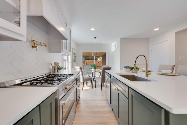 kitchen featuring sink, light hardwood / wood-style flooring, appliances with stainless steel finishes, hanging light fixtures, and decorative backsplash