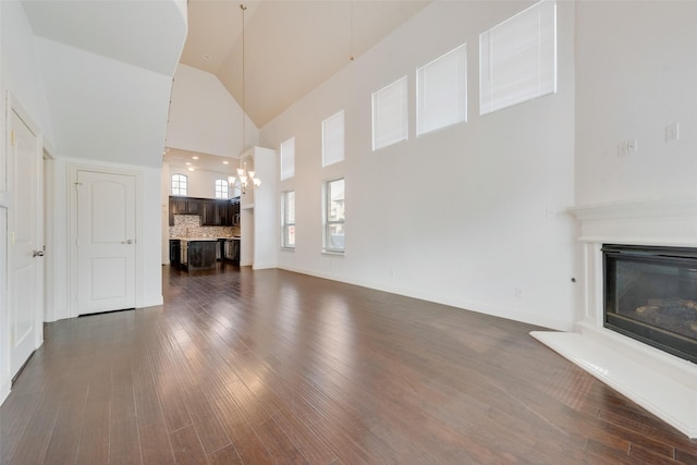 unfurnished living room featuring an inviting chandelier, dark hardwood / wood-style flooring, and a high ceiling