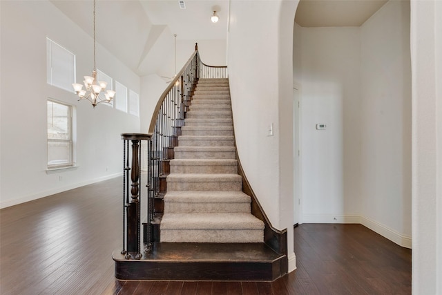 stairs with an inviting chandelier, a towering ceiling, and hardwood / wood-style flooring