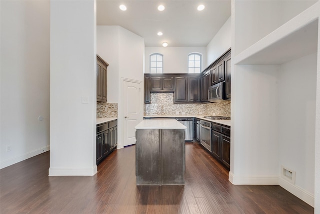 kitchen with appliances with stainless steel finishes, backsplash, dark brown cabinets, a center island, and dark wood-type flooring