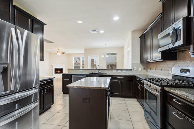 kitchen with sink, a kitchen island, stainless steel appliances, light tile patterned flooring, and decorative light fixtures