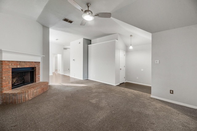 unfurnished living room featuring ceiling fan, vaulted ceiling, a brick fireplace, and dark colored carpet