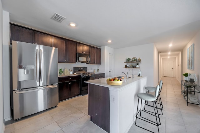 kitchen featuring light tile patterned flooring, a breakfast bar area, dark brown cabinetry, and black appliances