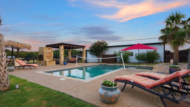 pool at dusk featuring a gazebo, an outdoor stone fireplace, and a patio