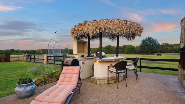 patio terrace at dusk with exterior kitchen, area for grilling, a yard, and a bar