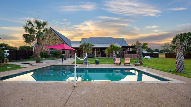 pool at dusk with a water slide, a patio area, and a lawn