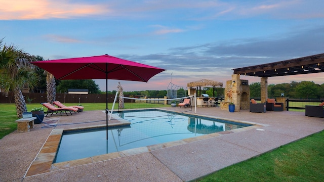 pool at dusk featuring exterior fireplace, a yard, and a patio