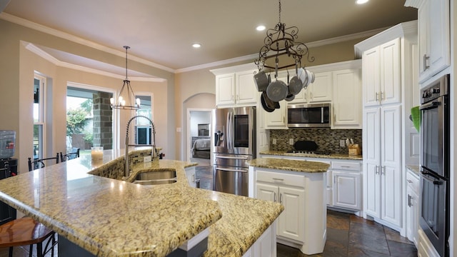 kitchen with a kitchen island with sink, decorative light fixtures, white cabinets, and appliances with stainless steel finishes