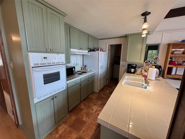 kitchen with tile counters, white appliances, under cabinet range hood, green cabinetry, and a sink