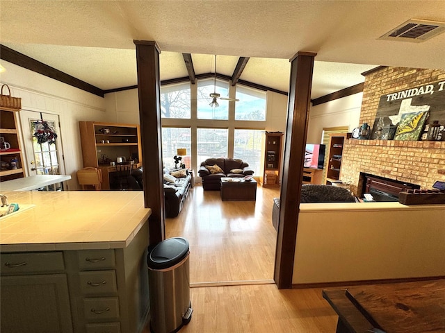 kitchen with lofted ceiling with beams, visible vents, open floor plan, light wood-type flooring, and tile counters