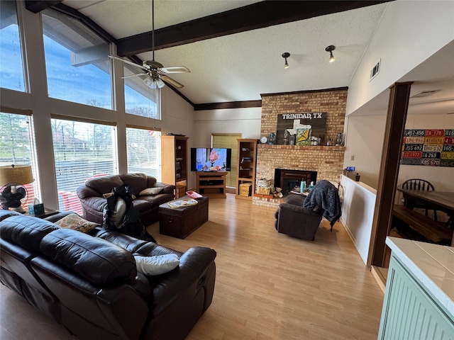 living room featuring light wood finished floors, visible vents, a textured ceiling, a fireplace, and beam ceiling