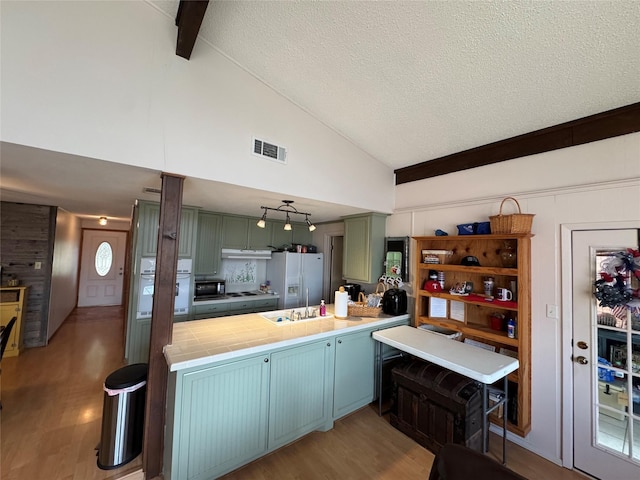 kitchen with a textured ceiling, a peninsula, white appliances, visible vents, and light wood-type flooring