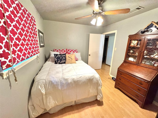 bedroom with visible vents, light wood-type flooring, a textured ceiling, and ceiling fan