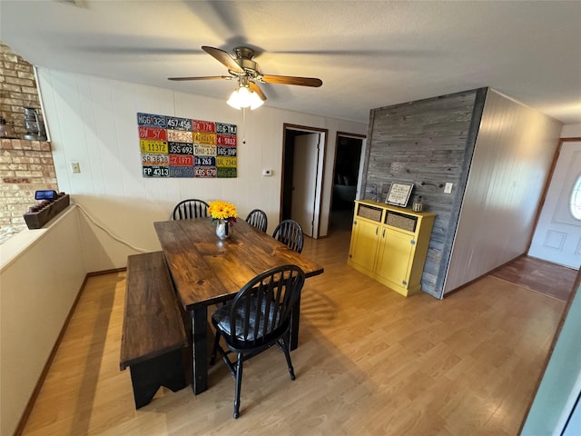 dining space featuring ceiling fan, light wood-type flooring, and wood walls