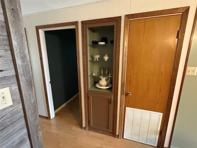 hallway with built in shelves, visible vents, wooden walls, light wood-type flooring, and baseboards