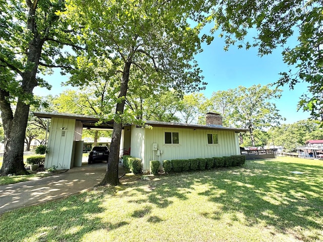 exterior space featuring a front yard, concrete driveway, an attached carport, and a chimney