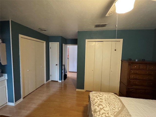 bedroom with ceiling fan, wood finished floors, two closets, and visible vents