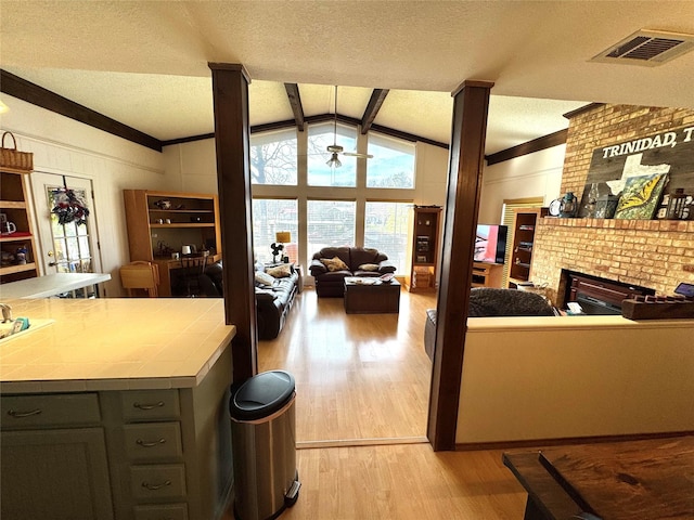 living room with a fireplace, visible vents, vaulted ceiling with beams, and light wood-style flooring
