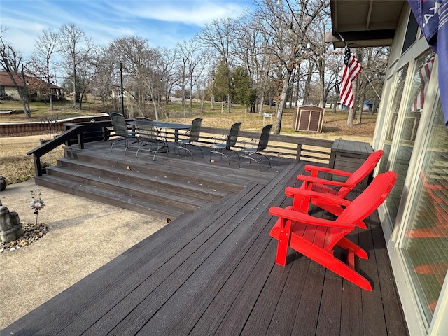 wooden terrace with outdoor dining space, an outbuilding, and a storage unit