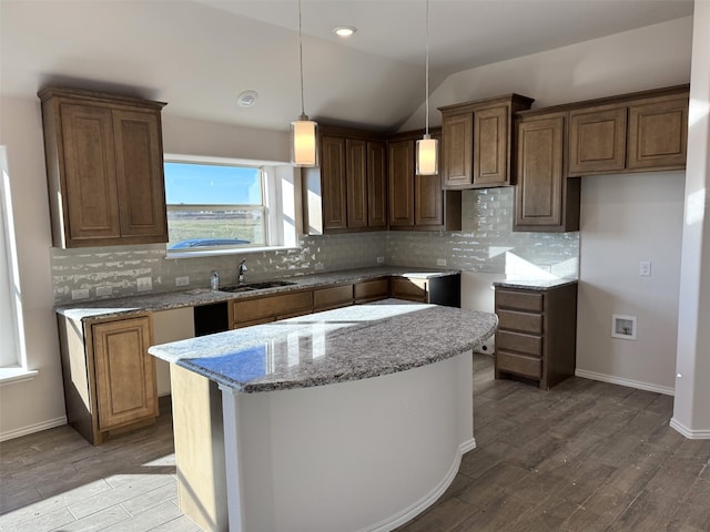 kitchen with lofted ceiling, sink, light stone counters, and a kitchen island