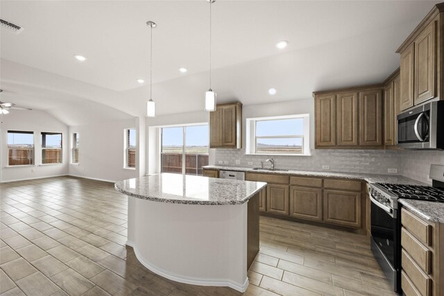 kitchen featuring ceiling fan, appliances with stainless steel finishes, backsplash, a center island, and light stone countertops