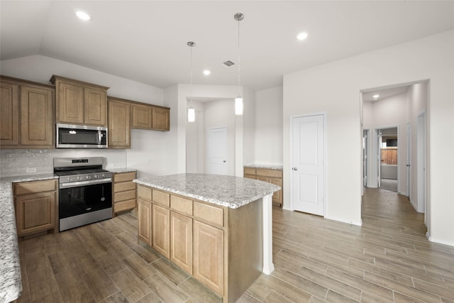 kitchen featuring lofted ceiling, appliances with stainless steel finishes, hanging light fixtures, a center island, and light stone counters