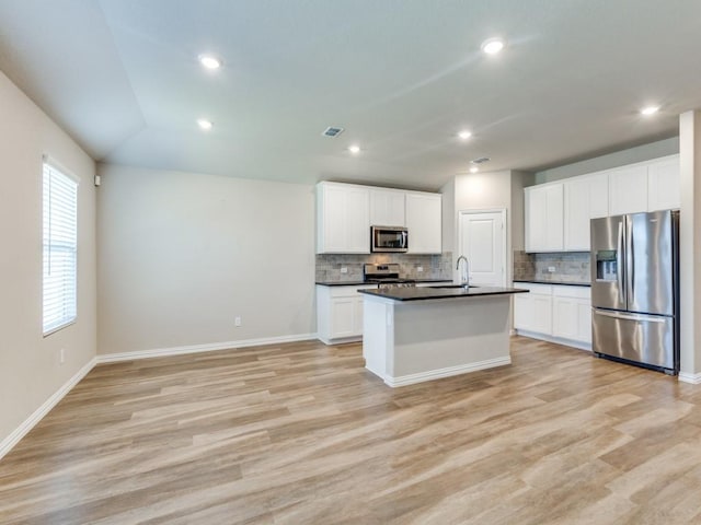 kitchen with a kitchen island with sink, backsplash, white cabinets, and appliances with stainless steel finishes