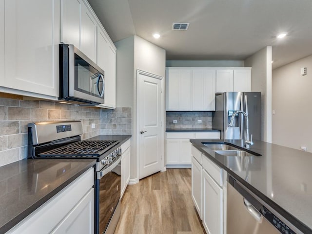 kitchen with sink, backsplash, white cabinets, stainless steel appliances, and light wood-type flooring